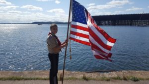 A Boy Scout holding the flag next to the Lower Harbor